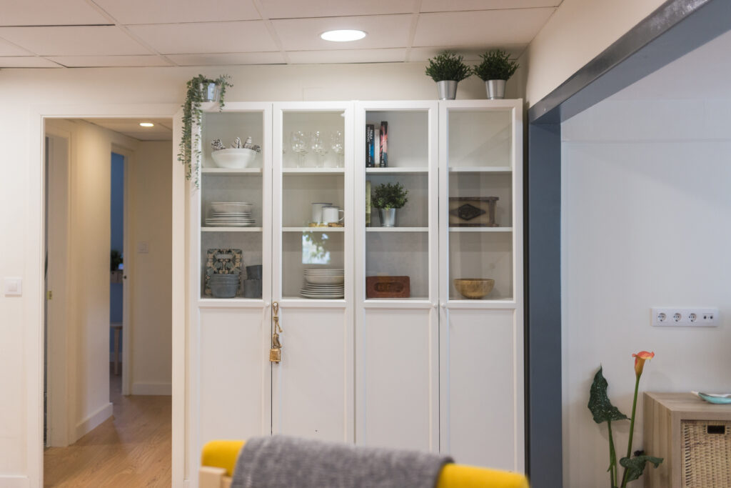 Vitrina blanca con vajilla y objetos decorativos junto al pasillo