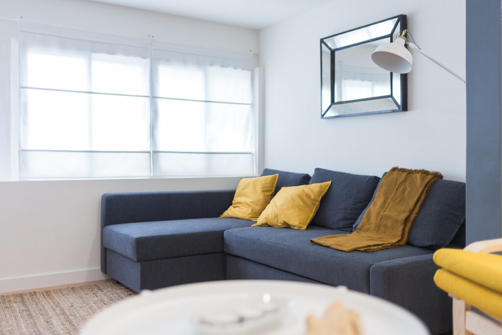 Salón con sofá azul, cojines mostaza y espejo en la pared