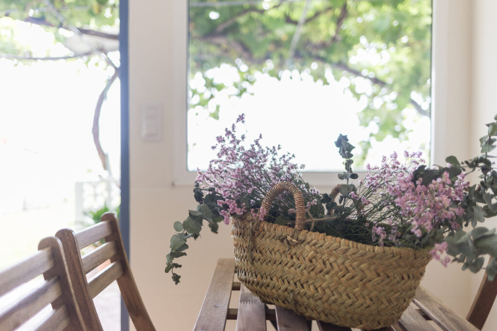 Cesta con flores secas sobre una mesa de madera, junto a una ventana de la casa