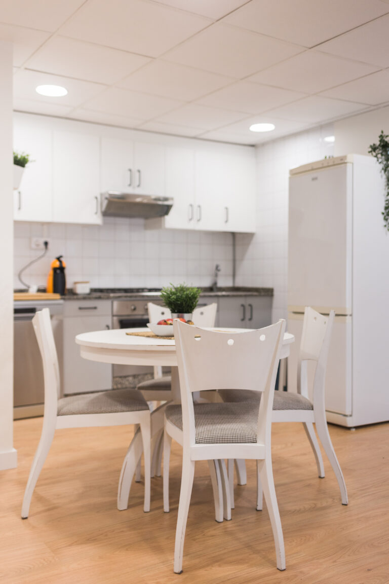 Mesa y sillas blancas en la cocina, con nevera al fondo
