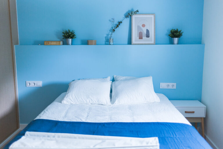 Dormitorio de matrimonio con pared azul y estantería decorativa