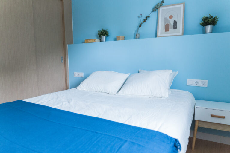 Dormitorio con cama de matrimonio, pared azul claro y mesita de noche